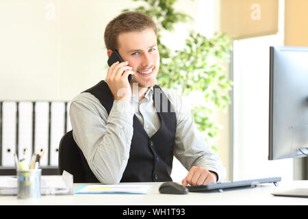 Felice executive parlando al telefono cercando in telecamera seduta in ufficio Foto Stock