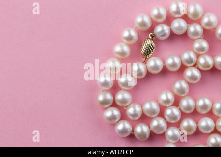 Collana di perle con chiusura in oro su sfondo rosa - vista superiore di perle rosa in rosa Foto Stock