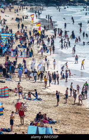 I turisti in vacanza in vacanza su una spiaggia Fistral soleggiata e affollata a Newquay in Cornovaglia. Foto Stock