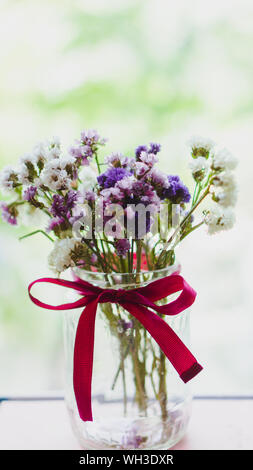 Un bouquet di viola appassita, rosa e bianco sono fiori di campo in un vaso trasparente con un colore rosso brillante prua. Fiori luminosi illuminate dalla luce del sole. Selettivo morbido Foto Stock