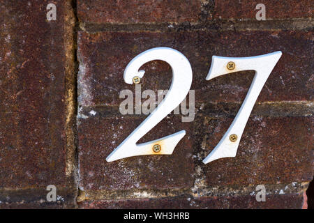 Casa bianca numero 27 su un vecchio muro di mattoni Foto Stock