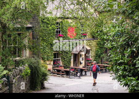 Uomo che cammina verso il basso una tranquilla stradina che conduce al Sun Inn storico pub e hotel. Coniston, Cumbria, Regno Unito, Gran Bretagna Foto Stock