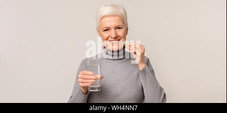 Bella donna anziana prendendo supplementi di vitamina sulla luce di sfondo per studio Foto Stock