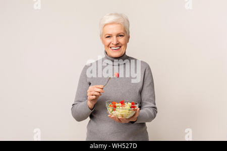 Donna senior di mangiare verdura fresca insalata sulla luce di sfondo per studio Foto Stock