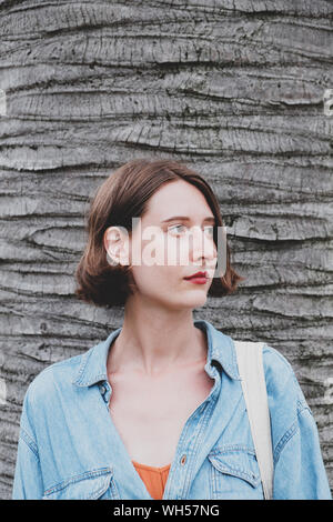 Donna in posa nella parte anteriore del palm tree trunk. Ritratto femminile sul corpo di un albero tropicale sfondo Foto Stock