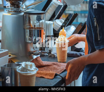 Il barista prepara bevande estive. Questa bevanda contiene espresso, latte freddo, cubetti di ghiaccio, panna e sciroppo. Si tratta di un drink estivo. Caffetteria, cucina. Foto Stock