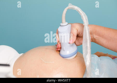 Ecografista la scansione di giovane donna incinta di addome con trasduttore a ultrasuoni esecuzione di ostetricia gravidanza o procedura di ultrasuoni Foto Stock