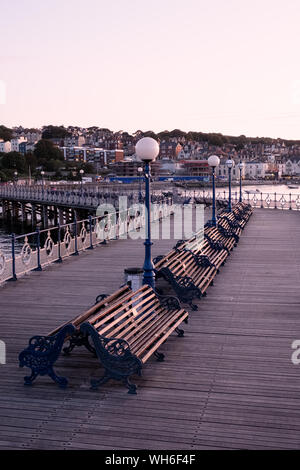 File di panche sul vecchio molo vittoriano, Swanage al tramonto. Foto Stock