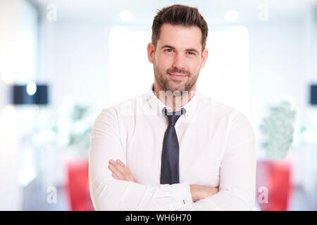 Ritratto di imprenditore sorridente indossando camicia e cravatta permanente, mentre in ufficio e sorridente. Foto Stock