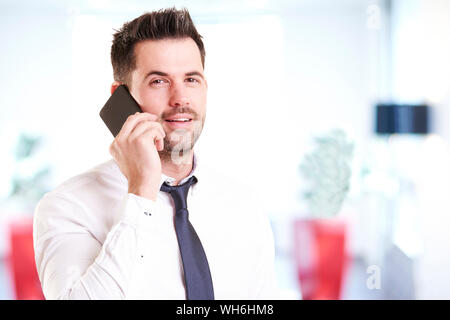 Ritratto di giovane uomo che guarda la fotocamera e sorridenti mentre si parla con qualcuno sul suo telefono cellulare. Foto Stock