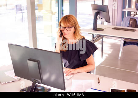 Colpo di executive imprenditrice seduto alla scrivania in ufficio e dare una chiamata mentre si lavora in ufficio. Foto Stock