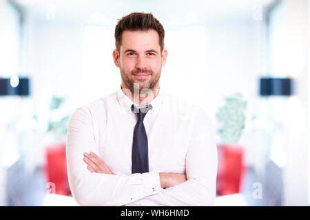 Ritratto di imprenditore sorridente indossando camicia e cravatta permanente, mentre in ufficio e sorridente. Foto Stock