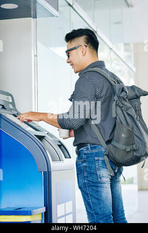 Positivo il vietnamita studente di college con zaino prelevare denaro dal terminale di banca Foto Stock