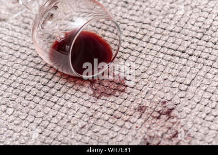 Il vetro con il vino rosso sul pavimento, rosso vino versato su un tappeto, macchie e chiazze di bevanda, close-up Foto Stock