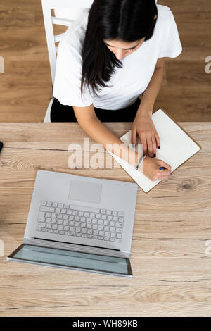 Vista superiore della giovane donna con il computer portatile prendere note Foto Stock