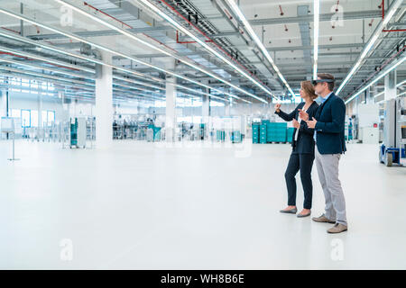 Imprenditore con AR bicchieri e imprenditrice in una fabbrica hall Foto Stock