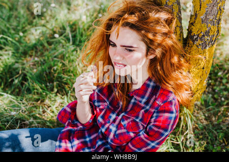 Ritratto di donna redheaded avente pausa sigaretta sotto un albero