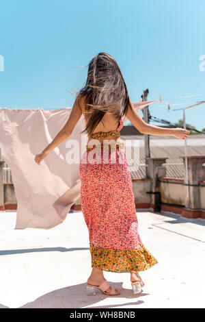 Vista posteriore della donna che indossa di moda top e gonna ballando sul tetto Foto Stock