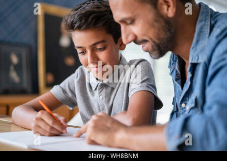 Padre sorridente aiutando figlio di fare i compiti di scuola Foto Stock