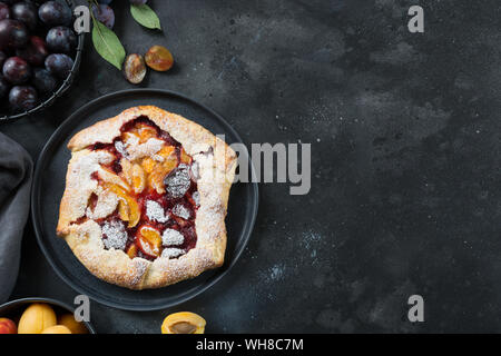 Fatta in casa torta galette con prugna e albicocca con prugna fresca rami sulla tavola nera. Vista da sopra. Orientamento orizzontale. Copia dello spazio. Foto Stock