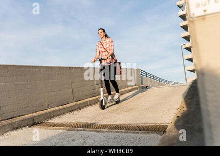 Giovane donna di equitazione scooter elettrico sul ponte di parcheggio Foto Stock