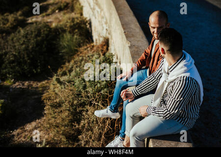 Coppia gay seduto su una parete tenendo le mani Foto Stock