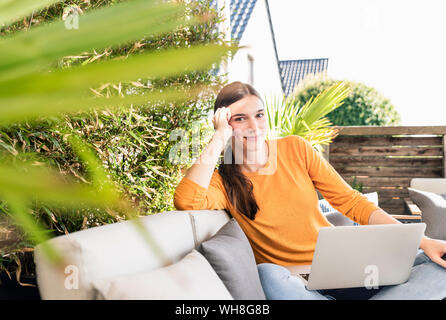 Ritratto di giovane sorridente donna seduta sulla terrazza con il computer portatile Foto Stock