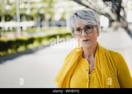 Ritratto di donna matura con i capelli grigi con gli occhiali e abiti di colore giallo Foto Stock