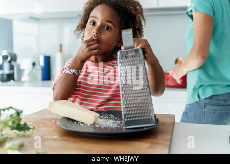 Ragazza la cottura con la madre in cucina degustazione di formaggio grattugiato Foto Stock