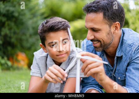 Sorridente padre e figlio giacente in giardino con una turbina eolica modello Foto Stock