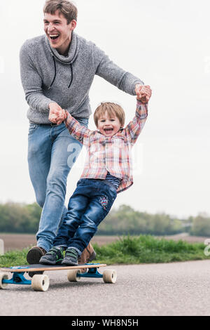 Padre e figlio divertirsi giocando con lo skateboard all'aperto Foto Stock