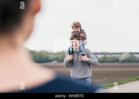 La famiglia felice camminando insieme accanto a campi, padre figlio portante sovrapponibile Foto Stock