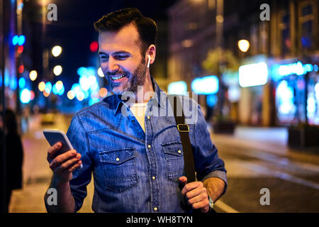 Uomo con cuffie wireless utilizza lo smartphone nella città di notte Foto Stock