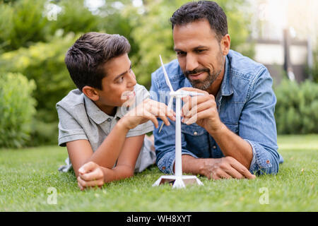 Sorridente padre e figlio giacente in giardino con una turbina eolica modello Foto Stock