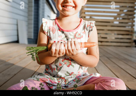 Bambina seduti sulla terrazza tenendo la carota, vista parziale Foto Stock