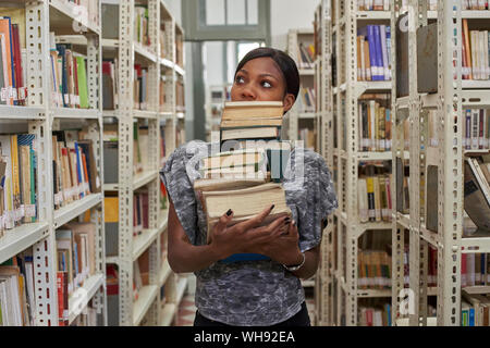 Giovane donna con la pila di libri alla biblioteca nazionale, Maputo Mocambique Foto Stock