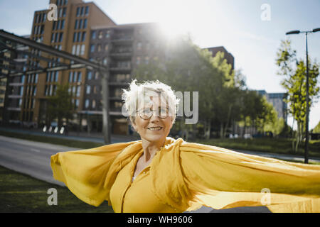 Ritratto di sorridere donna matura a retroilluminazione indossando abiti di colore giallo Foto Stock