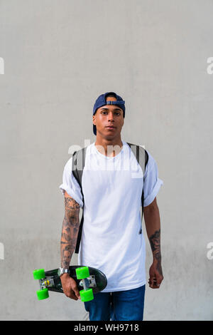 Ritratto di tatuati giovane con lo skateboard di fronte a uno sfondo grigio Foto Stock