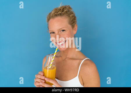 Sorridente donna bionda di bere succo di frutta, sfondo blu Foto Stock