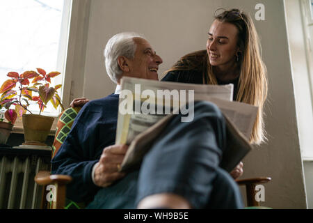 Felice giovane donna e uomo senior con quotidiano a casa Foto Stock