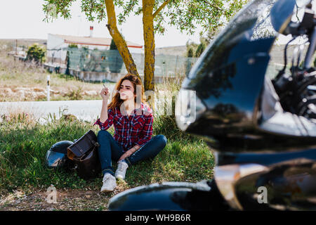 Motociclista aventi pausa sigaretta sotto un albero Foto Stock