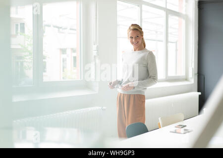 Sorridente giovane donna in piedi presso la finestra di office Foto Stock