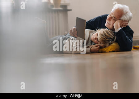 Nonno e nipote sdraiato sul pavimento di casa utilizzando un tablet Foto Stock