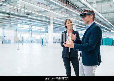 Imprenditore con AR bicchieri e imprenditrice in una fabbrica hall Foto Stock