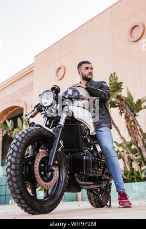 Ritratto di giovane uomo seduto sulla sua moto Foto Stock