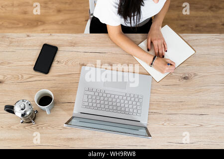 Vista superiore della giovane donna con il computer portatile prendere note Foto Stock