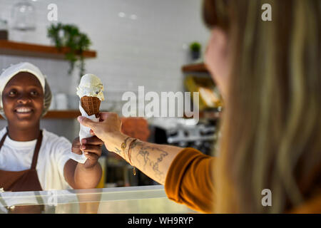 Giovane donna lavora in gelateria, consegnando il cono gelato per il cliente Foto Stock