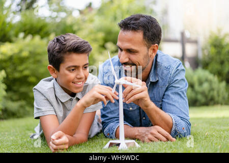 Sorridente padre e figlio giacente in giardino con una turbina eolica modello Foto Stock