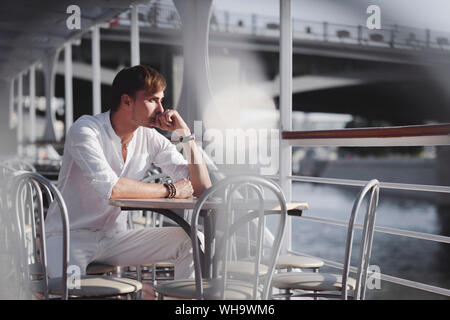 Malinconici uomo indossando vestiti di bianco seduto sulla barca per gite a luce del sole guardando a distanza, Mosca, Russia Foto Stock