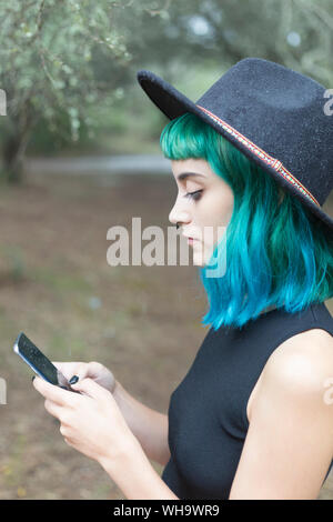 Profilo di giovane donna con tinti di blu e verde capelli utilizzando smartphone sul giorno di pioggia Foto Stock